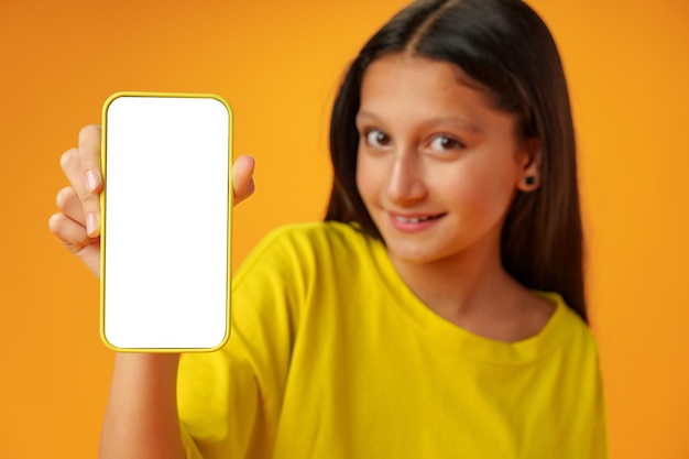 Teen girl showing smartphone screen with copy space over yellow background