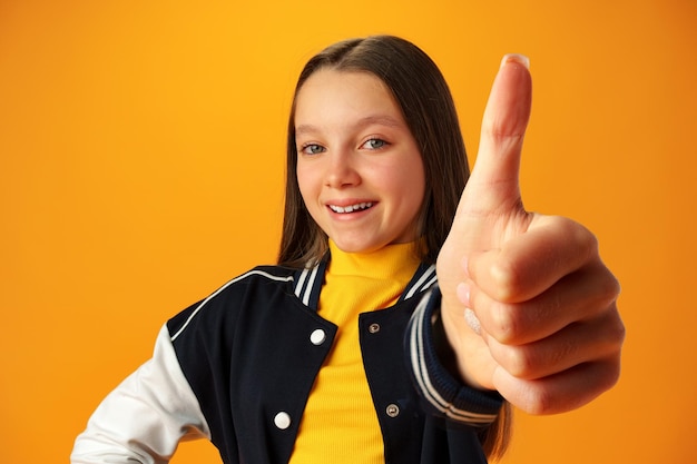 Teen girl showing thumb up sign against yellow background