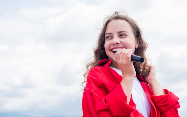 Ragazza teenager che canta una canzone nel microfono sullo sfondo del cielo, musica dal vivo.