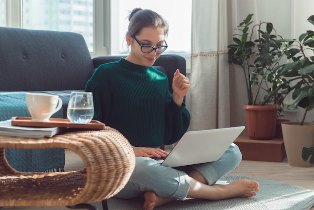 teen girl sits on sofa with laptop and drinks water