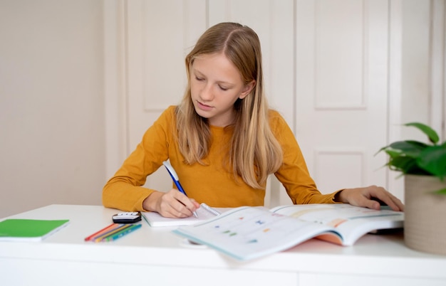 Photo teen girl sitting at table with book and pen doing homework