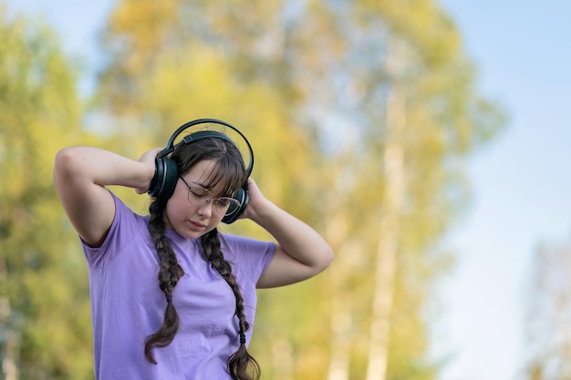 Photo a teen girl stands on the street, presses headphones to her ears with her hands and listens to music