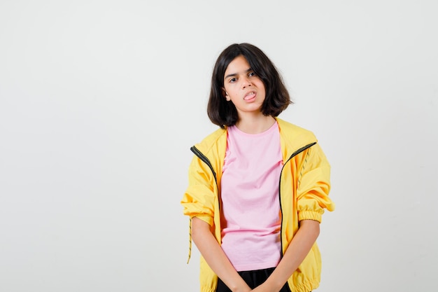 Teen girl sticking tongue out in t-shirt, jacket and looking bored , front view.