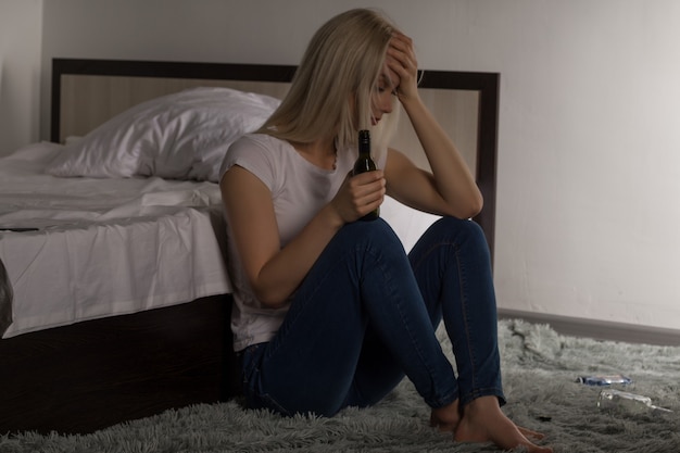 Teen girl suffering from a hangover while sitting on the floor near the bed in a student dormitory