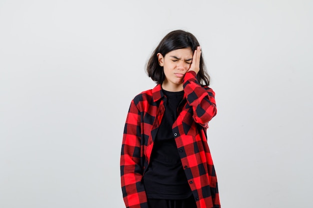Teen girl suffering from headache in t-shirt, checkered shirt and looking painful. front view.