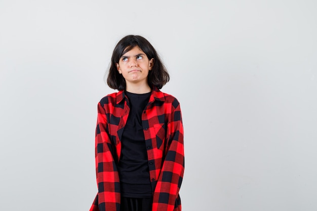 Teen girl in t-shirt, checkered shirt looking upward and looking thoughtful , front view.