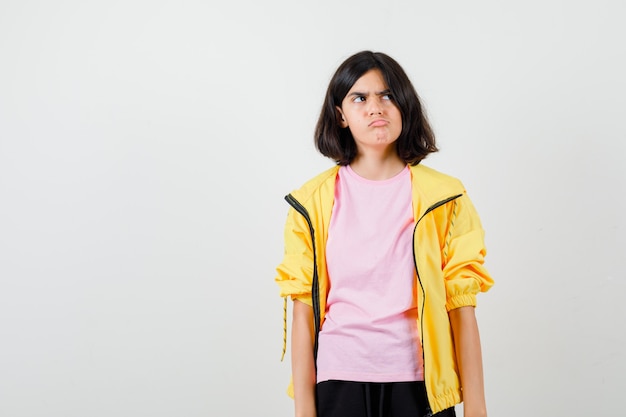 Ragazza teenager in t-shirt, giacca che curva il labbro inferiore, distoglie lo sguardo e sembra annoiata, vista frontale.