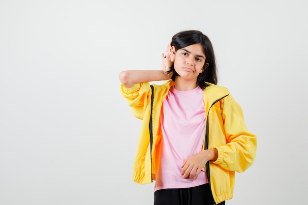 Teen girl in t-shirt, jacket keeping hand behind ear and looking upset , front view.