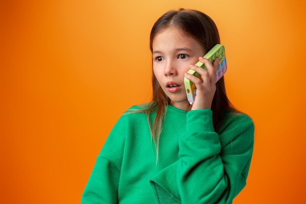 オレンジ色の背景で隔離の携帯電話で話している十代の少女