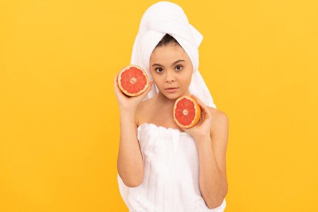 Девочка-подросток в полотенце с грейпфрутом на желтом фоне