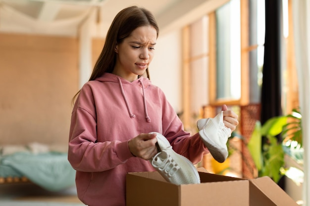 Teen girl unhappy with received sneaker shoes dissatisfied client opening box and looking at wrong delivered item