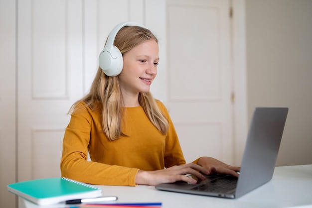 Teen girl using laptop and headphones at desk