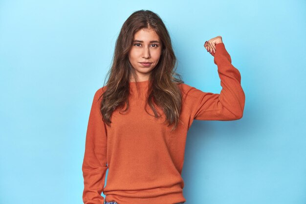 Teen girl in vibrant orange sweater on blue showing fist to camera aggressive facial expression