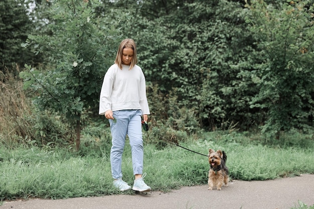 Foto ragazza teenager in una passeggiata nel parco estivo con il suo animale domestico yorkshire terrier. bambino che porta a spasso un cane