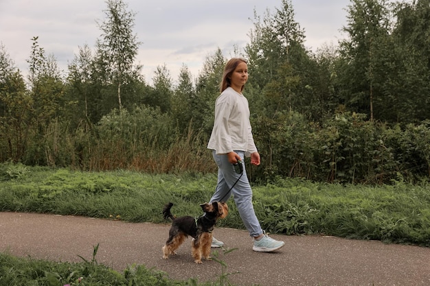 Teen girl on a walk in the summer park with her pet Yorkshire terrier. Child walking a dog