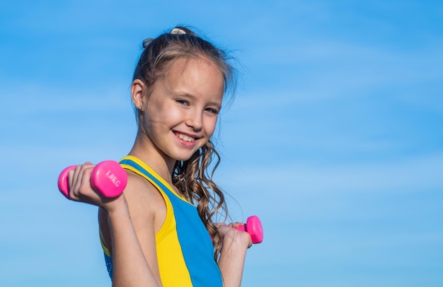 Teen girl wear sportswear for training with barbells on sky background copy space workout