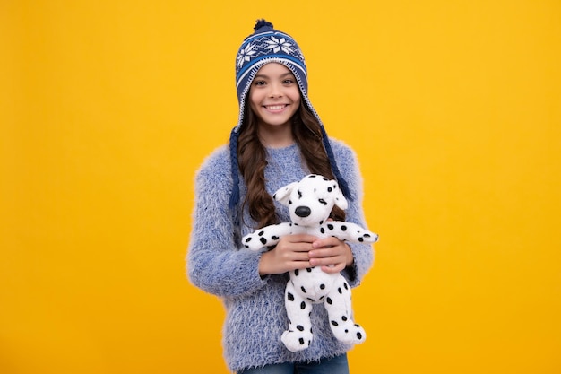Teen girl in in winter hat hold soft toy for birthday on yellow background Kid spending time with her toys Childhood toys and kids Happy child girl