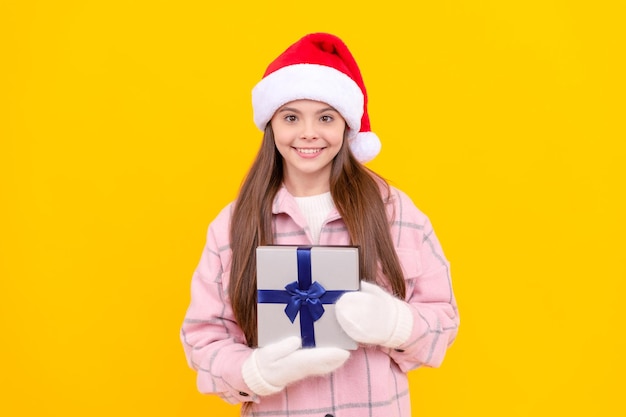 Teen girl in winter mittens on yellow background xmas holiday present child wearing warm clothes hold gift box happy new year merry christmas happy smiling kid in santa claus hat