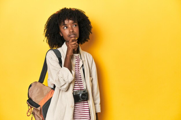 Teen girl with backpack camera ready for vacation looking sideways with doubtful