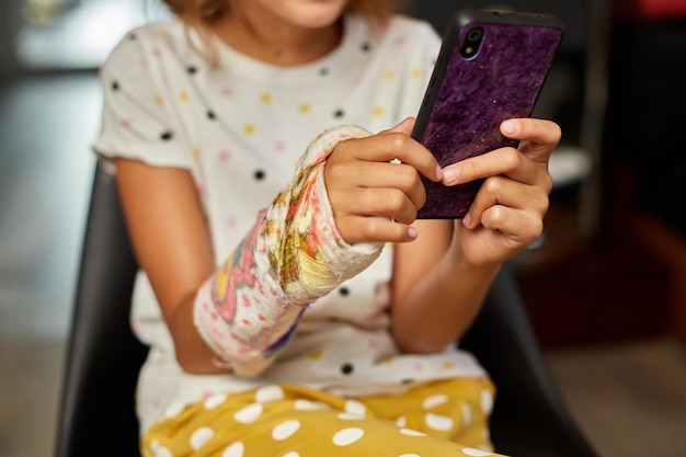 Teen girl with a broken arm orthopedic cast use smartphone