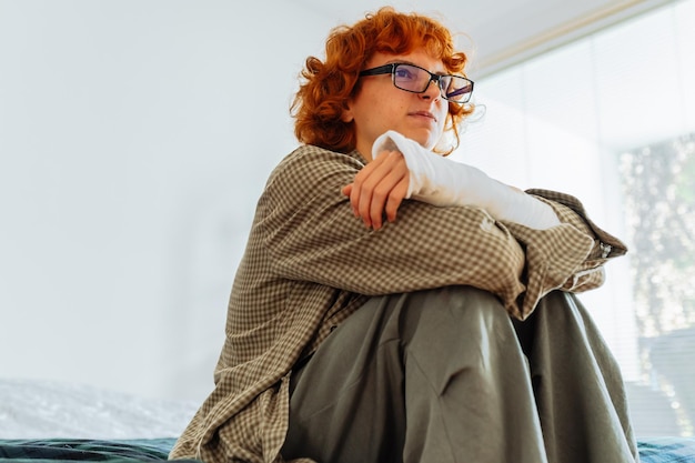 Teen girl with broken arm wearing glasses red hair in bedroom