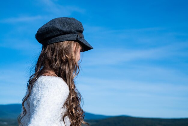 Teen girl with long curly hair wear trendy hat on sky background future