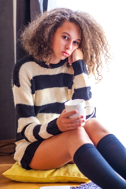 Teen girl with mug by window