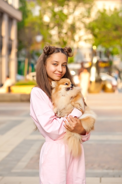 Teen girl with pet animal small dog holding in a hands outdoor in a park.