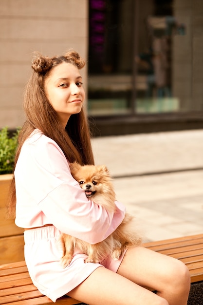 Девушка-подросток с домашним животным маленькая собачка держит в руках на открытом воздухе в парке