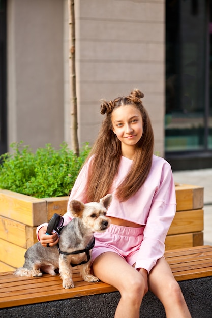 Teen girl with pet animal small dog sitting on a bench outdoor.