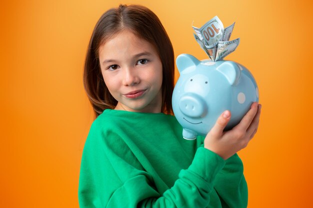 Teen girl with piggy bank on orange color background