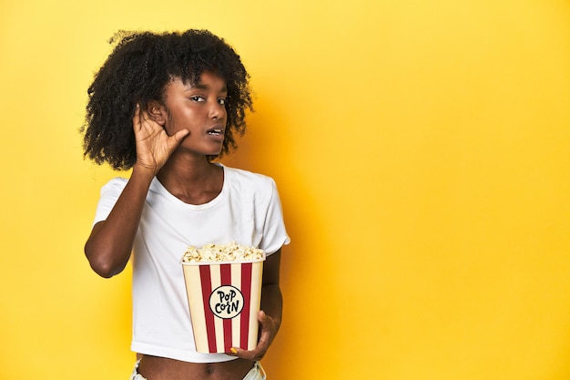 Photo teen girl with popcorn cinema concept on yellow backdrop trying to listening a gossip