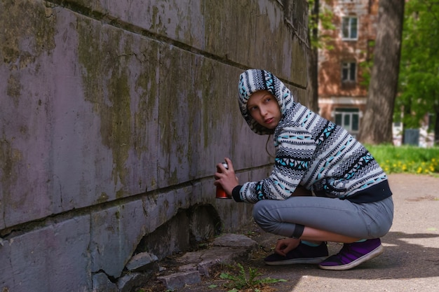 Photo teen girl with spray paint looks around, about to write graffiti on the wall