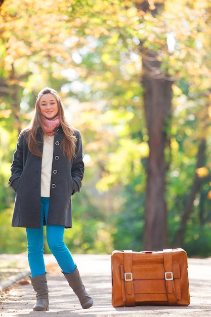 Девушка-подросток с чемоданом осенью на открытом воздухе