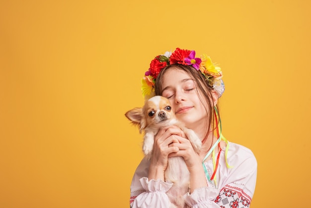 彼女の頭に花輪を持ち、チワワの白い犬と刺繡シャツを着た十代の少女