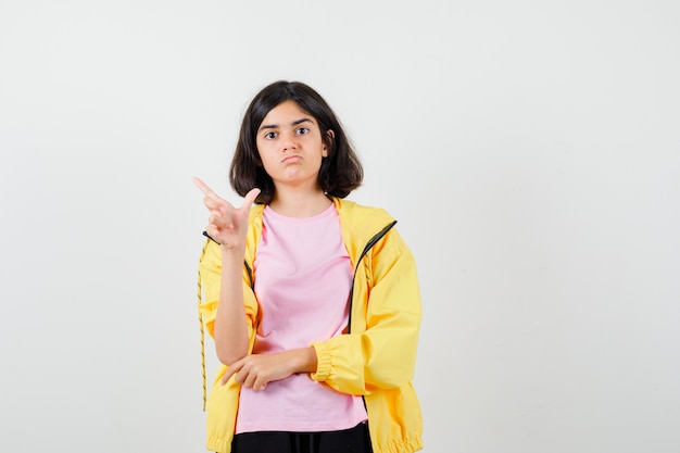 Teen girl in yellow tracksuit, t-shirt showing loser gesture and looking wistful , front view.