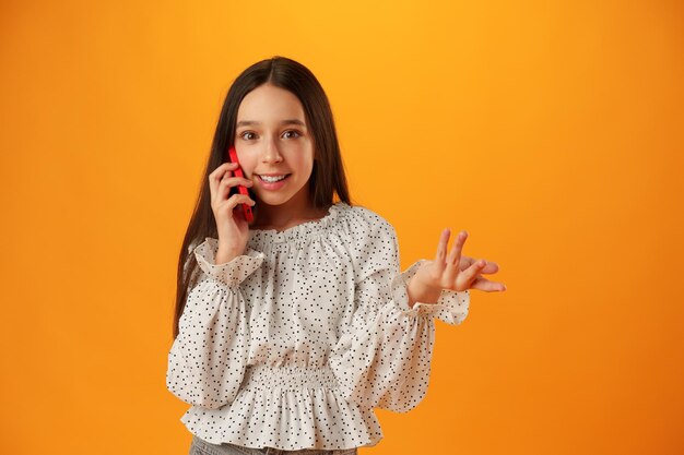 Foto ragazza adolescente sul muro giallo che parla sullo smartphone.