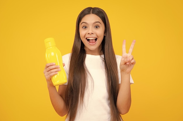 Teen holds water bottle isoalted on yellow Child girl care body hydration Active leisure and water balance Active and healthy kid drink water Excited teenager glad amazed and overjoyed emotions