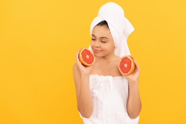 Teen kid in towel smell grapefruit on yellow background