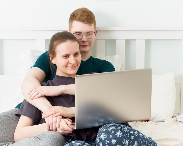 Teen in love lying on bed, watch movies on laptop during quarantine due to coronavirus pandemic