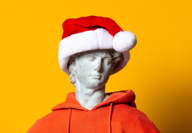 Teen sculpture in orange hoodie and Christmas hat on yellow background