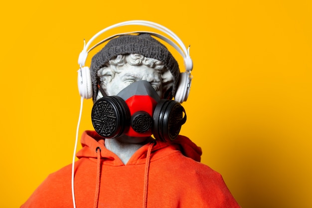 Teen sculpture in orange hoodie, face mask and hat with headphones on yellow background