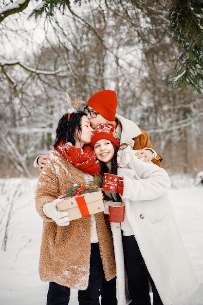 Братья и сестры-подростки и их мать стоят в зимнем парке с подарочной коробкой