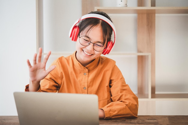 Teenage Asian students in a yellow dress wearing a headphone are communicating through video conferencing for online learning. In a video conference call via apps. new normal concept