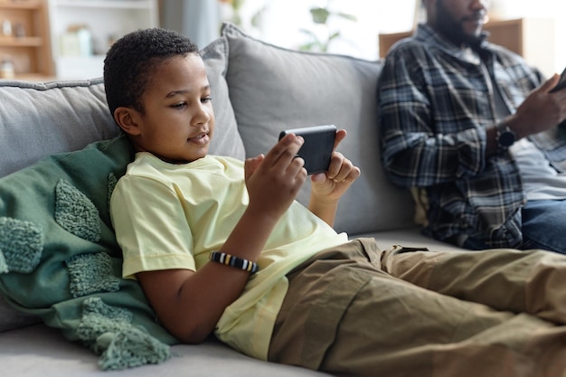 Чернокожий подросток пользуется смартфоном на диване.