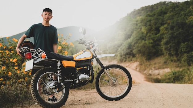 A teenage boy and a classic enduro motorcycle on a rocky road.