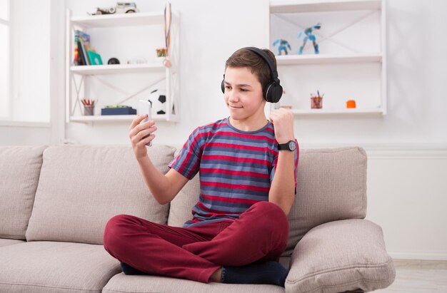 Teenage boy enjoying music in headphones at home. Making selfie and sharing with friends in social media, relax time