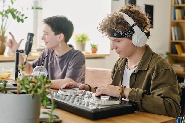 Teenage boy in headphones adjusting sound on turntables during stream