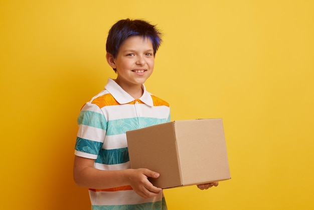 Teenage boy holding blank cardboard box over isolated yellow background delivery concept