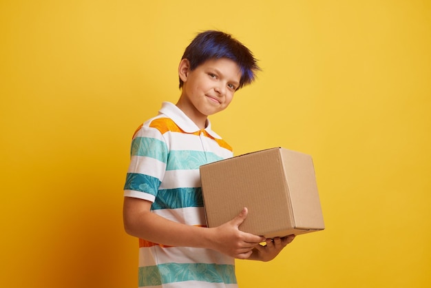 Teenage boy holding blank cardboard box over isolated yellow background delivery concept